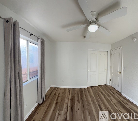 A room with a ceiling fan and a window with curtains.