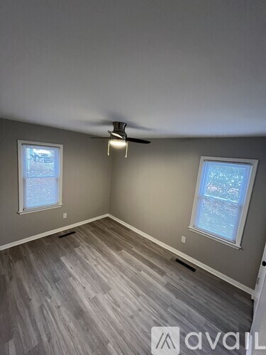 A room with a ceiling fan and two windows.