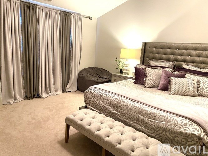 A bedroom with a large bed, a bench, and a window with curtains.