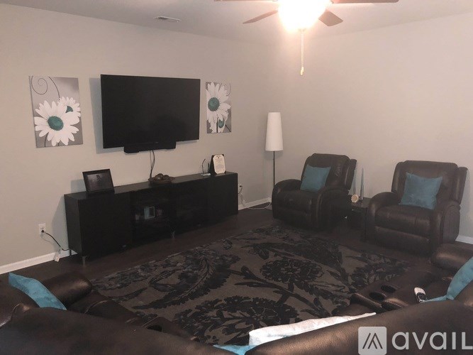 A living room with a black sofa, a television, and a ceiling fan.