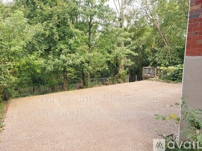 A gravel driveway leads to a wooded area with a sign that reads "All County Music City Property Management.".