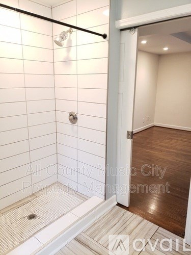 A bathroom with a tiled shower and a doorway leading to a hallway.