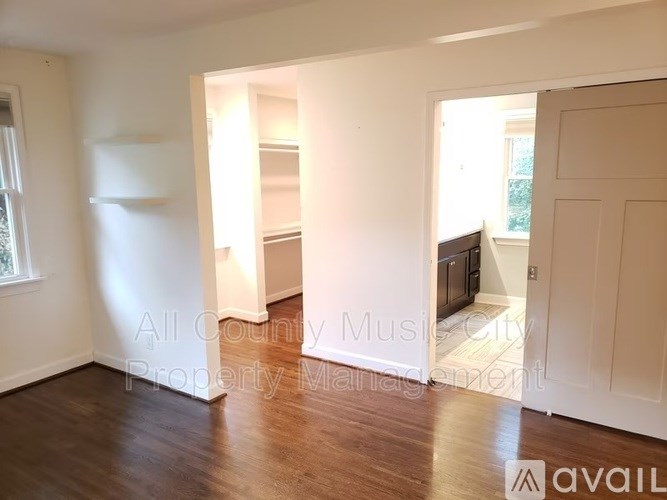 A room with wooden floors and white walls, with a doorway leading to another room.