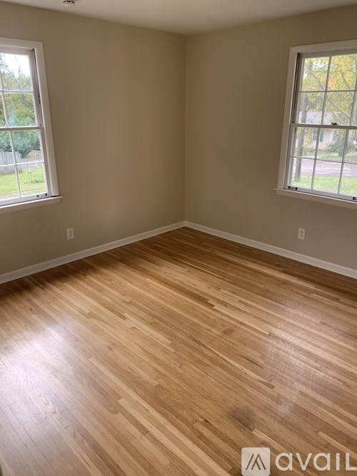 A room with wooden flooring and two windows.