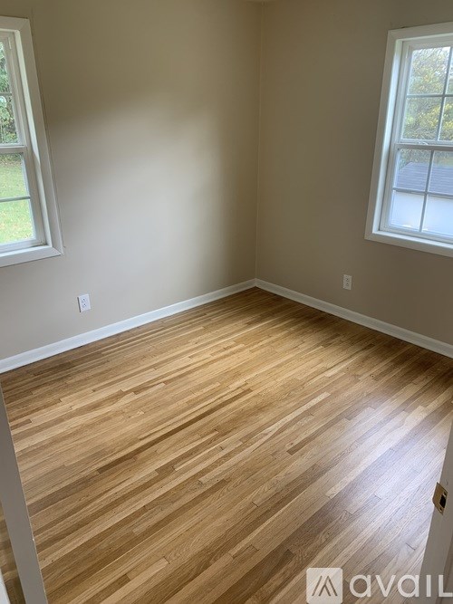 A room with wooden flooring and two windows.