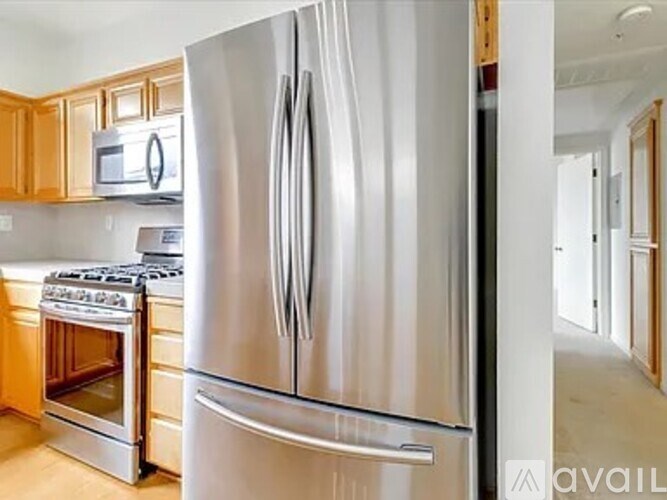 A stainless steel refrigerator stands in a kitchen with wooden cabinets and a microwave.