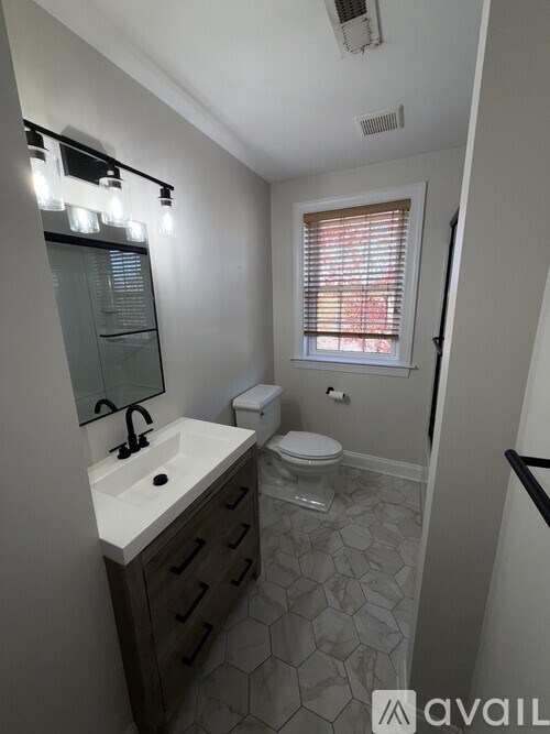 A bathroom with a sink, toilet, and a window with blinds.