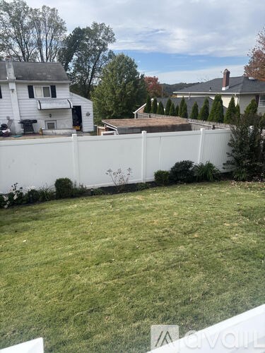 A white fence separates a yard from a house.