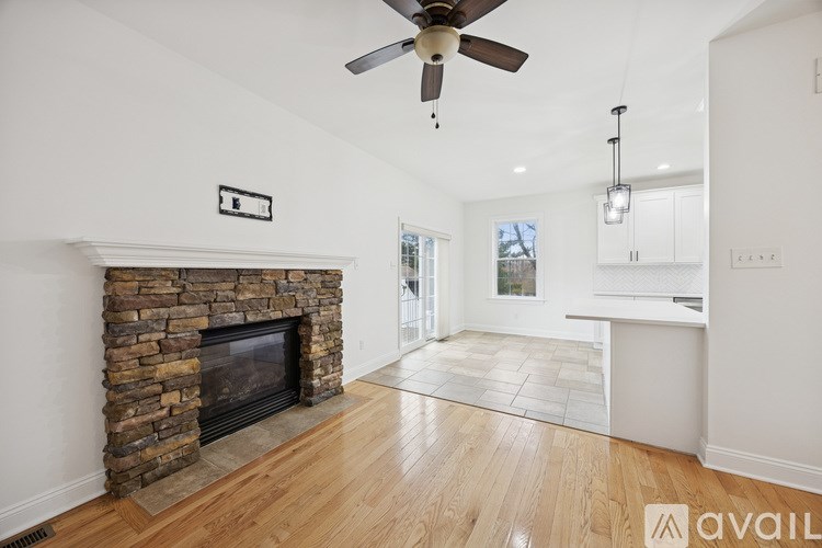 A living room with a stone fireplace and a ceiling fan.