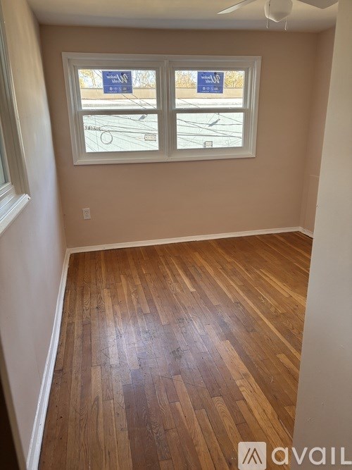 A room with wooden flooring and a window with a view of a parking lot.