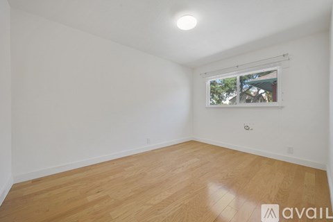 A room with wooden flooring and a window showing trees outside.