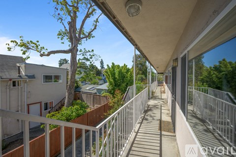 A balcony with a metal railing and a tree in the background.