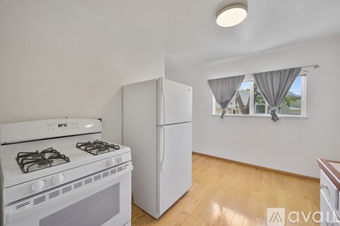 A white kitchen with a stove, refrigerator, and wooden floors.