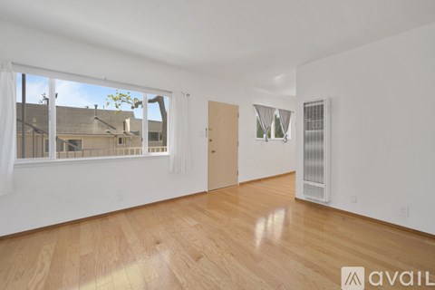 A spacious room with wooden flooring and a large window overlooking a residential area.
