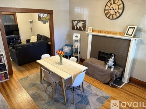 A cat is sitting on a grey couch in a living room with a wooden table and chairs.