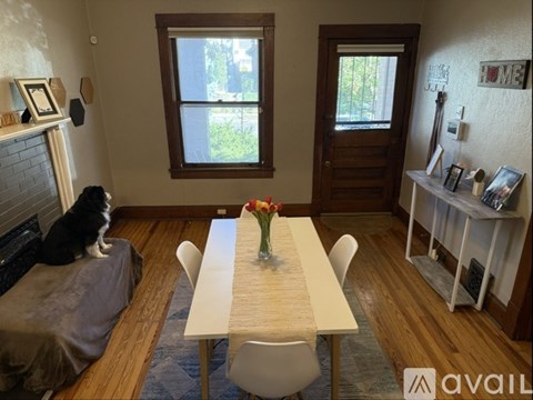 A cat is sitting on a grey couch in a room with a wooden table and chairs.
