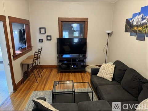 A living room with a black couch, a glass coffee table, a flat screen TV, and a wooden floor.