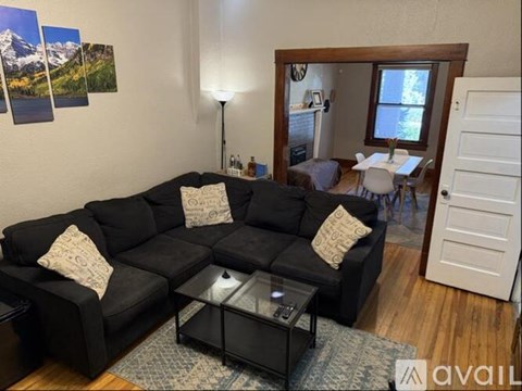 A black sectional sofa with a glass coffee table in the middle of a living room.