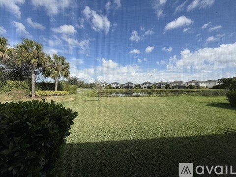 A grassy field with trees and houses in the distance under a blue sky.