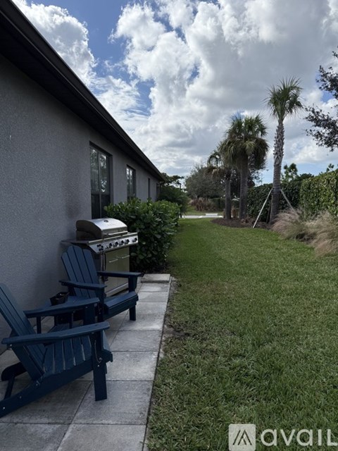 A blue Adirondack chair sits on a concrete patio next to a grill.
