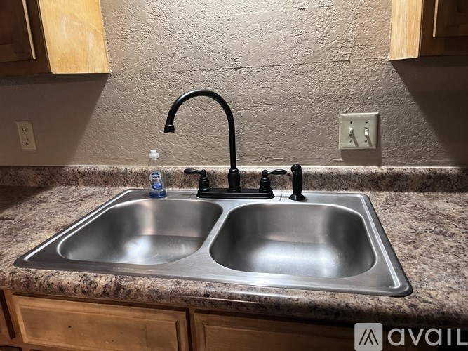 A kitchen sink with a black faucet and a bottle of water on the counter.