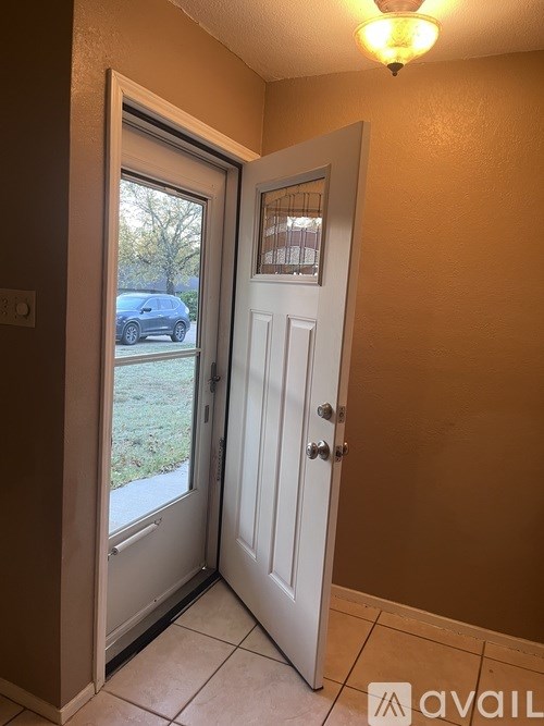 A white door is open to a patio with a car parked in the background.
