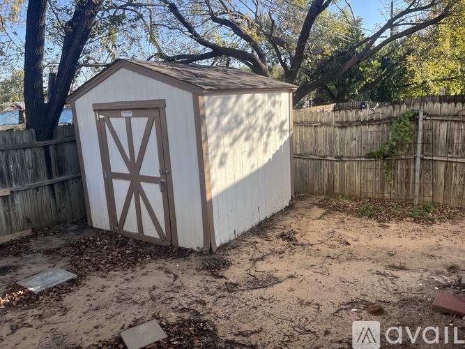 A small white shed with a brown door is situated in a backyard.