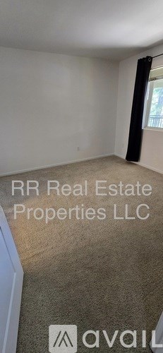 A room with a carpeted floor and a window with a black curtain.
