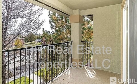 A balcony with a black railing and a view of a street and trees.