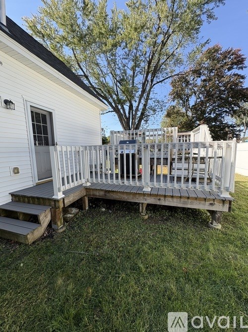 A white house with a deck and a tree in the background.