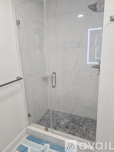 A white bathroom with a glass shower stall and a marble floor.