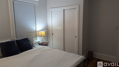 A bedroom with a bed, pillows, a nightstand with a lamp, and a door.