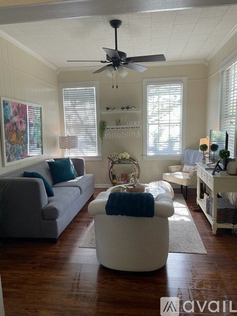 A living room with a grey couch, a white ottoman, and a ceiling fan.