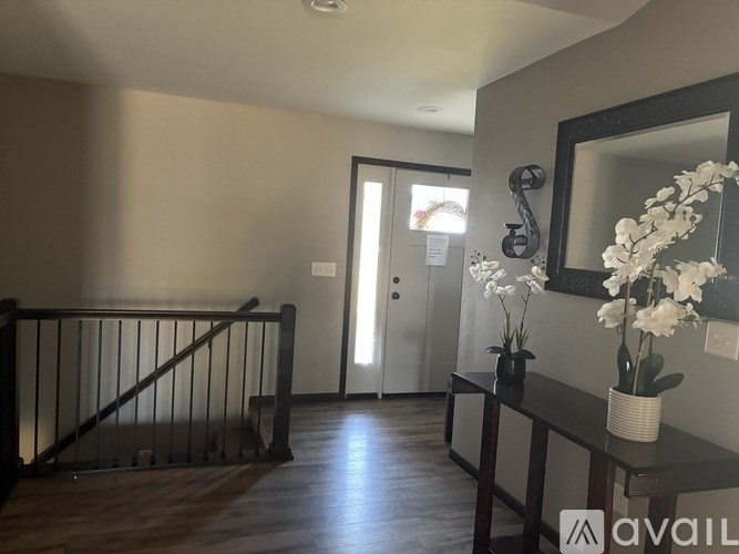 A hallway with a wooden floor, a mirror, and a vase of white flowers.