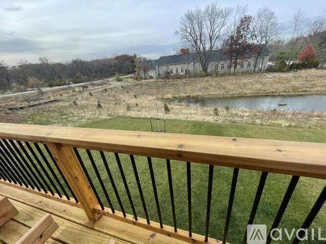 A wooden deck overlooks a field with a house in the distance.