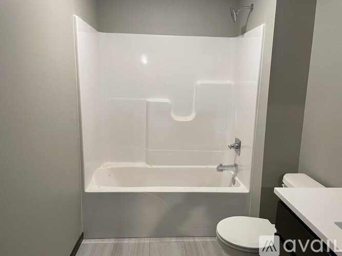 A white bathtub with a shower head is in a bathroom with a toilet and sink.