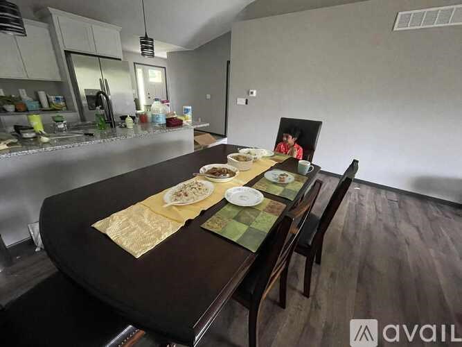 A dining table set with plates and napkins is in the foreground of a kitchen.