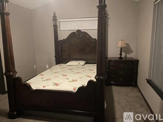 A bed with a wooden frame and a floral bedspread sits in a room with a lamp and a dresser.