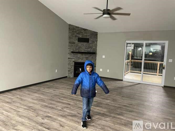 A boy in a blue jacket is standing in a room with a ceiling fan.