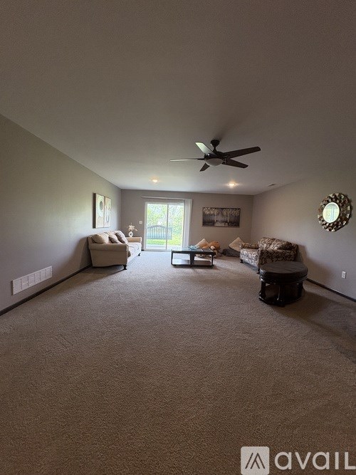 A living room with a carpeted floor and a ceiling fan.