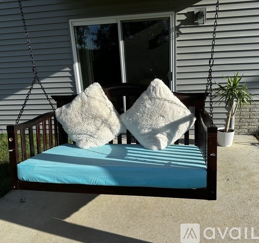 A porch swing with two large white pillows is hanging from a chain.