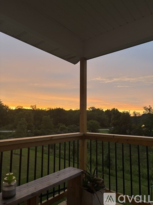 A wooden bench sits on a porch with a view of a sunset.