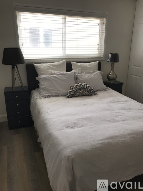 A bedroom with a white bed and a black dresser.