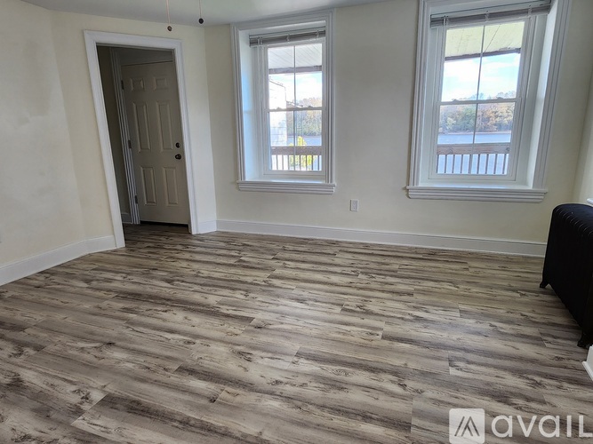 A room with wooden flooring and two windows.