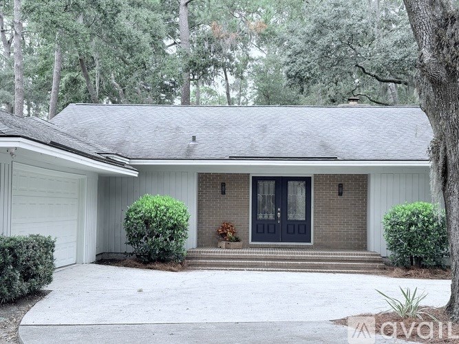 A house with a dark blue front door is surrounded by greenery.