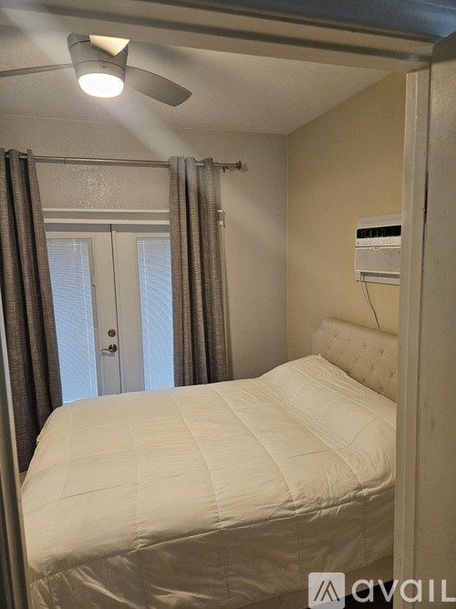 A bedroom with a bed, a window with curtains, and a ceiling fan.