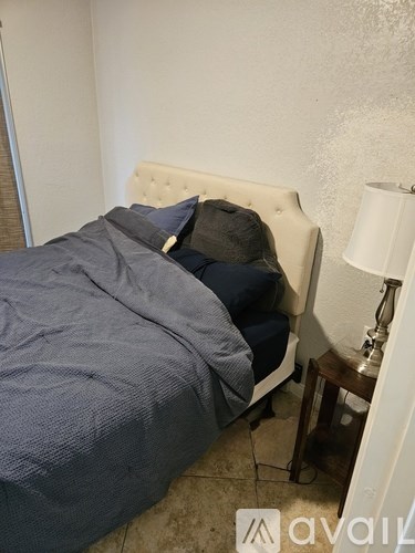 A bed with a white headboard and blue bedding is in a room with a lamp on a small table.