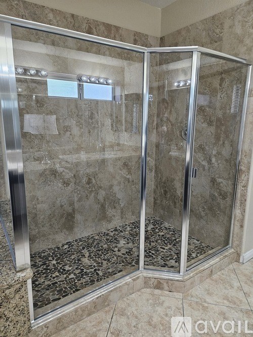 A shower with a glass door and a marble floor.