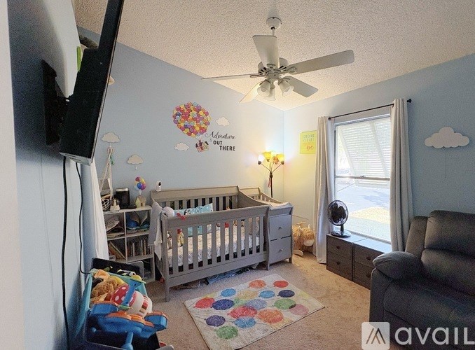 A baby's room with a crib, a dresser, a fan, and a colorful rug.