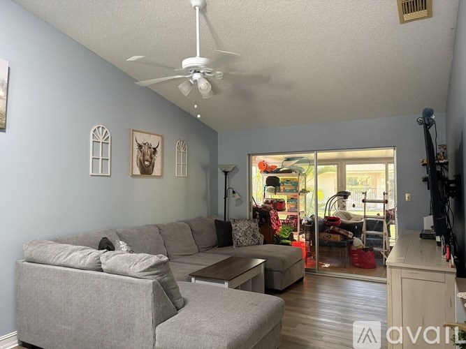 A living room with a grey couch and a white ceiling fan.